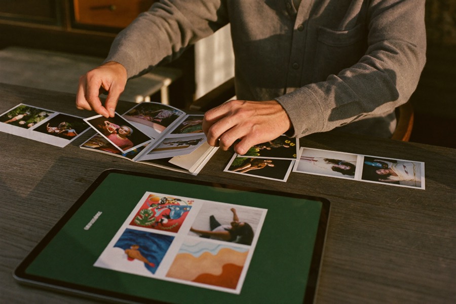 Hände ordnen gedruckte Fotos neben einem Tablet – ein Fotobuch entsteht